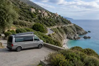 Van aménagé stationné près d’un camping sur une route côtière du Cap Corse, avec un village, le maquis et une crique en arrière-plan.
